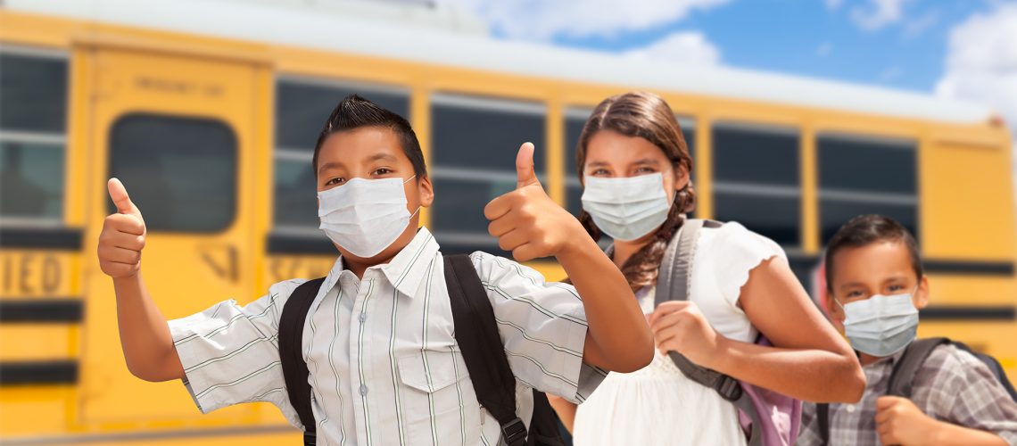 Hispanic Students Near School Bus Wearing Face Masks.